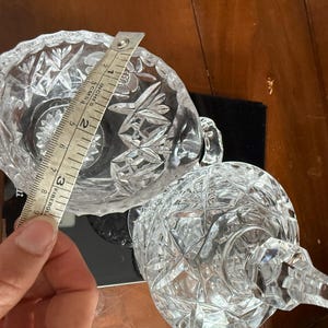 May include: Clear crystal sugar bowl and a stemmed glass with a diamond pattern. The sugar bowl is approximately 3 inches (7.6 cm) in diameter. The objects are on a dark surface.