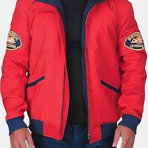 以下が含まれることがあります： 赤色のベイウォッチライフガードジャケット。ネイビーブルーの襟、袖口、ポケットトリムが特徴。ベイウォッチライフガードのロゴが入った2つのパッチとジッパー開閉部があります。