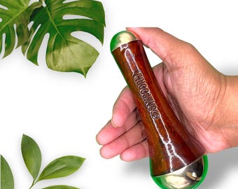May include: A wooden face roller with gold-toned metal ends. The roller is held in a hand and has the word "WOODWISE" engraved on the side.