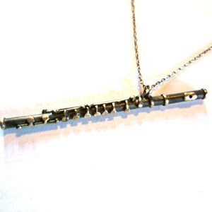 Puede incluir: Un collar con un colgante de flauta de plata. La flauta est&aacute; detallada con llaves de plata y una cadena de plata.