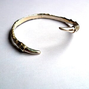 May include: A silver bangle bracelet with a textured, organic design. The bracelet has a pointed end and is open on one side.
