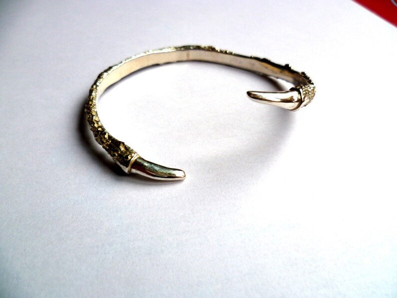 May include: A silver bangle bracelet with a textured, organic design. The bracelet has a pointed end and is open on one side.