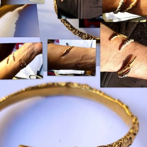 May include: A gold bangle bracelet with a textured surface and two claw-like ends. The bracelet is open and has a rounded shape.
