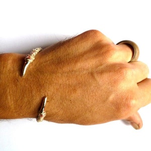 May include: A gold-toned bracelet with a claw-like design. The bracelet is worn on a person's wrist.