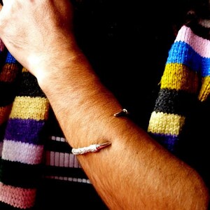 May include: A silver bracelet with a pointed end, worn on a person's arm. The person is wearing a colorful striped sweater.