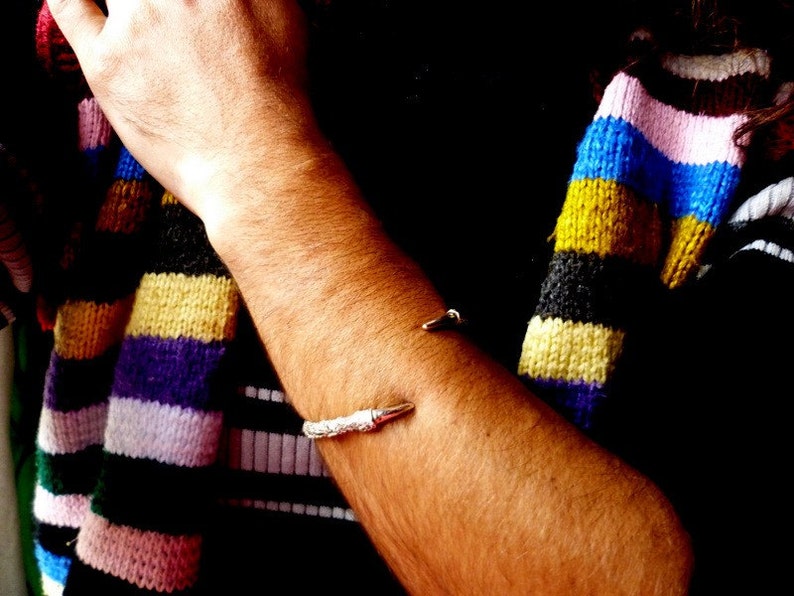 May include: A silver bracelet with a pointed end, worn on a person's arm. The person is wearing a colorful striped sweater.