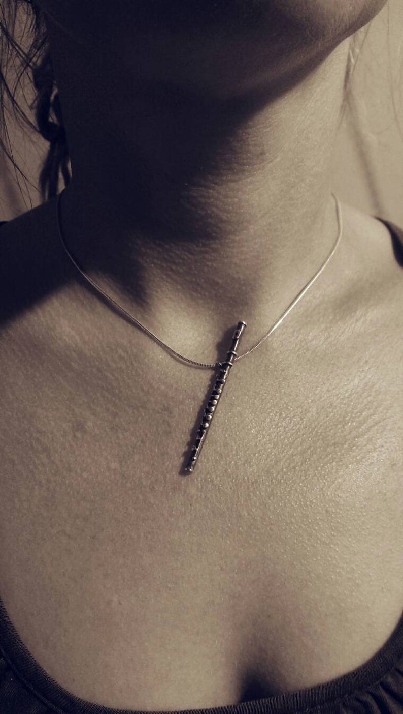 Puede incluir: Un collar de plata con un colgante de flauta. La flauta est&aacute; hecha de metal y tiene un dise&ntilde;o detallado.