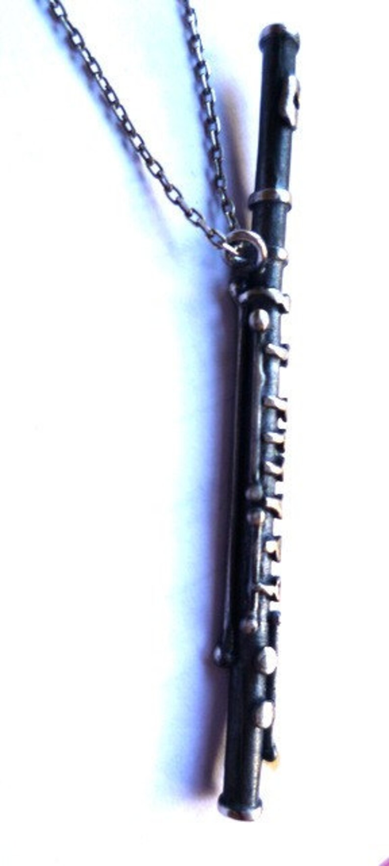 Puede incluir: Un collar de cadena de plata con un colgante de plata con forma de clarinete. El clarinete est&aacute; detallado con llaves de plata y una boquilla de plata.