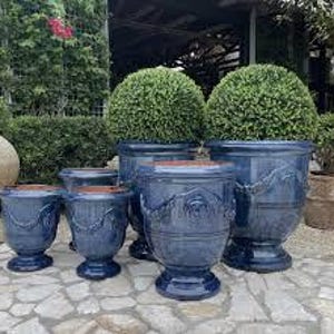 May include: A selection of blue ceramic plant pots of different sizes, displayed on a stone surface. Each pot has a textured finish and rope-style detailing. The pots are filled with green, spherical plants.