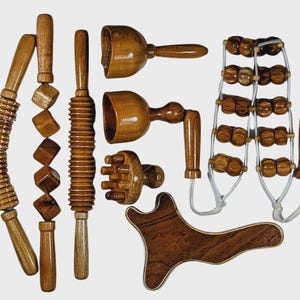 Puede incluir: Colección de herramientas de masaje de madera, que incluyen rodillos, masajeadores y una herramienta gua sha. Las herramientas tienen varias formas y tamaños, todas hechas de madera de tono medio cálido. La disposición sugiere bienestar.