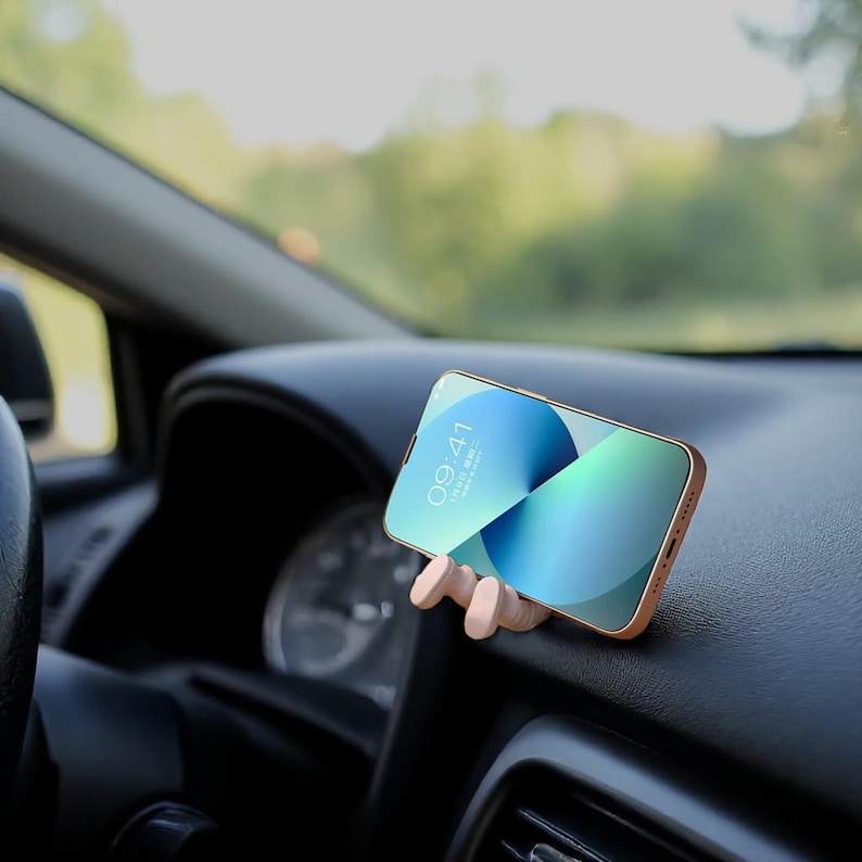 Op de afbeelding: Een goudkleurige smartphone met de tijd 09:41 wordt in een houten telefoonhouder in een auto gehouden. Het scherm van de telefoon toont een blauw-groene gradi&euml;nt. Het dashboard en het stuur zijn zichtbaar op de achtergrond.