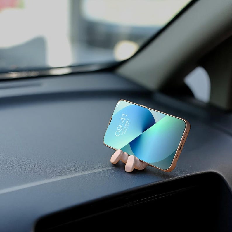 Op de afbeelding: Een smartphone met een blauwgroen scherm rust in een houten telefoonhouder op het dashboard van een auto. De telefoon geeft de tijd 09:41 weer. De houder is lichtbruin en heeft een minimalistisch ontwerp.