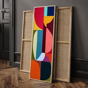 Puede incluir: Un cuadro rectangular alto de lienzo con una composición geométrica de semicírculos y bloques superpuestos en colores vibrantes que incluyen rojo, amarillo, azul cerceta, naranja, azul oscuro, rosa y verde oliva, enmarcado en madera clara.