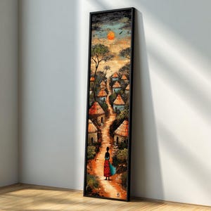 以下が含まれることがあります： アフリカの村の風景を描いた、縦長の額装されたアートワーク。絵画は、茅葺き屋根の小屋を通る小道が夕焼けへと続く様子を描いています。カラフルなドレスを着た人物が小道に立っています。アートワークは白い壁に展示されています。