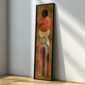Puede incluir: Impresión artística abstracta en un marco negro. La obra presenta una serie de círculos y arcos superpuestos en tonos de rojo, marrón, verde y beige sobre un fondo dorado. La pieza rectangular vertical está apoyada contra una pared blanca.