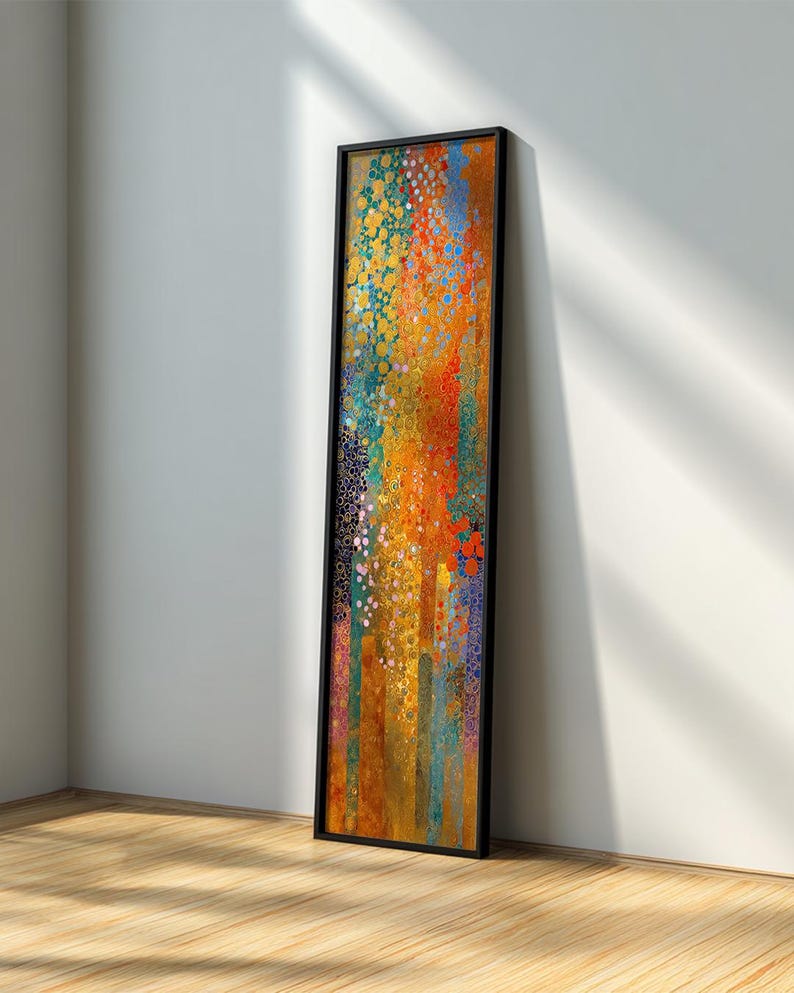 May include: A long, vertical framed art piece with an abstract design. The artwork features a vibrant mix of colors, including orange, yellow, blue, and green, with a textured, dotted pattern. The frame is black, and the piece is leaning against a white wall.