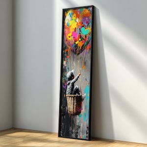 May include: A framed vertical art print depicts a child in a wicker basket, holding strings attached to a colorful hot air balloon. The balloon is a vibrant mix of colors, including yellow, orange, pink, and blue. The artwork has a modern, abstract style.