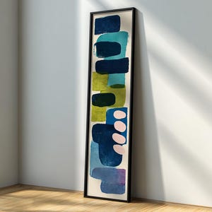 May include: Vertical abstract art print in a black frame. The artwork features layered rectangular shapes in shades of blue, green, and pink against a cream background. The piece is leaning against a white wall and a wooden floor.