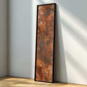 May include: A tall, rectangular wall art piece featuring a heavily textured, oxidized metal surface with deep shades of rust, burnt orange, and dark brown, enclosed within a thin, solid black frame that provides a sharp, clean border.