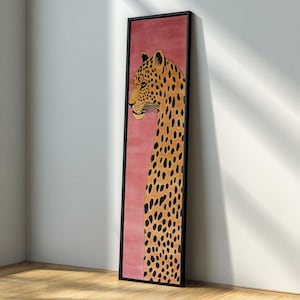 May include: A framed artwork featuring a leopard illustration. The leopard is depicted in profile with a long neck and spotted coat. The background is a solid pink colour, and the frame is black.