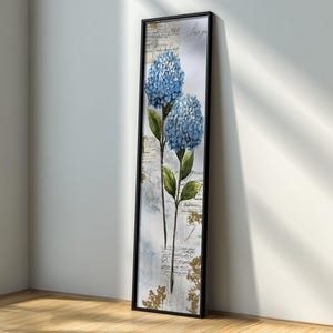 May include: A tall, rectangular framed wall art piece featuring two blue hydrangea flower clusters with green leaves. The background consists of a collage of vintage-style script handwriting, faded paper textures, and subtle gold-toned floral accents.