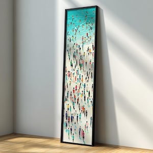May include: A framed vertical art print depicting a beach scene with numerous figures in colorful attire. The artwork features a turquoise ocean, a sandy shore, and a multitude of people, creating a vibrant and lively composition. The frame is black.