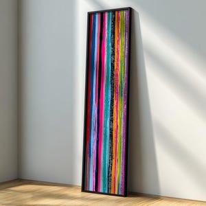 Könnte beinhalten: Vertikales abstraktes Kunstwerk mit schwarzem Rahmen. Das Kunstwerk zeigt farbenfrohe vertikale Streifen in Pink, Blau, Grün, Orange und Schwarz. Es lehnt an einer weißen Wand auf einem Holzboden.