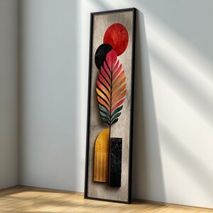 May include: Abstract wall art featuring a colorful feather design with red, black, and orange accents. The artwork is framed in a black rectangular frame and includes a red circle and a yellow arch. The piece is displayed against a neutral background.