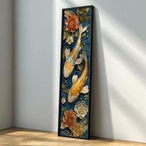 Op de afbeelding: Een ingelijst kunstwerk met twee koi-karpers met gouden en witte schubben, tegen een blauwe achtergrond met bloemendetails. Het stuk bevat oranje, witte en gele bloemen en is ingesloten in een zwart frame.