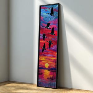 May include: A vertical framed artwork depicts a sunset scene with a flock of geese in flight. The sky transitions from blue to red and orange, with a yellow sun setting over a body of water. The geese are black with white markings.