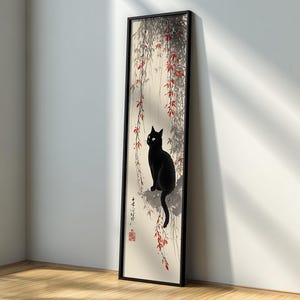 May include: A framed art print featuring a black cat perched on a branch, set against a backdrop of stylized foliage with red accents. The artwork is in a vertical format, with a black frame, and is leaning against a white wall.