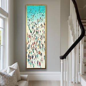 May include: Vertical framed artwork depicting a beach scene with numerous figures. The top portion shows a turquoise ocean with swimmers, transitioning to a white sandy beach filled with people in various colorful outfits. The artwork is encased in a gold frame.