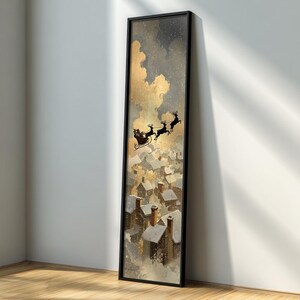 May include: A framed vertical art print depicts Santa's sleigh pulled by reindeer flying over a snowy village. The artwork features a black frame, a gold and gray sky, and detailed rooftops.
