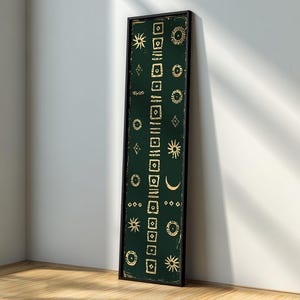 May include: A tall, rectangular framed wall art piece featuring a dark forest green background with a vertical central column of gold square symbols. Flanking this column are various gold celestial icons, including suns, moons, and stars.