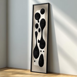 Puede incluir: Obra de arte abstracta en blanco y negro enmarcada. El diseño presenta una serie de formas orgánicas negras sobre un fondo neutro. La obra enmarcada se apoya en una pared blanca sobre un suelo de madera, creando una estética moderna. El marco es negro.