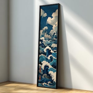 Puede incluir: Una impresión vertical enmarcada que representa una escena oceánica estilizada con grandes olas en tonos azules y blancos. La obra de arte presenta un cielo azul oscuro con nubes blancas y esponjosas. El marco es negro y la impresión está apoyada contra una pared blanca.