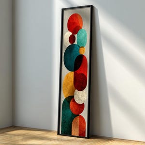 May include: Vertical abstract art print featuring a stack of colorful, textured circles in red, teal, yellow, and white, set against a neutral background. The artwork is framed in a black rectangular frame, adding a modern touch to the design.