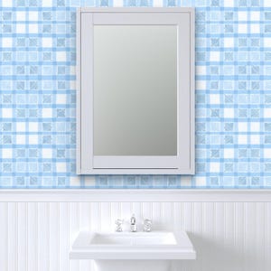May include: A white framed mirror is mounted on a wall with blue and white plaid wallpaper. Below the mirror is a white sink with a chrome faucet. The lower wall has white vertical paneling.