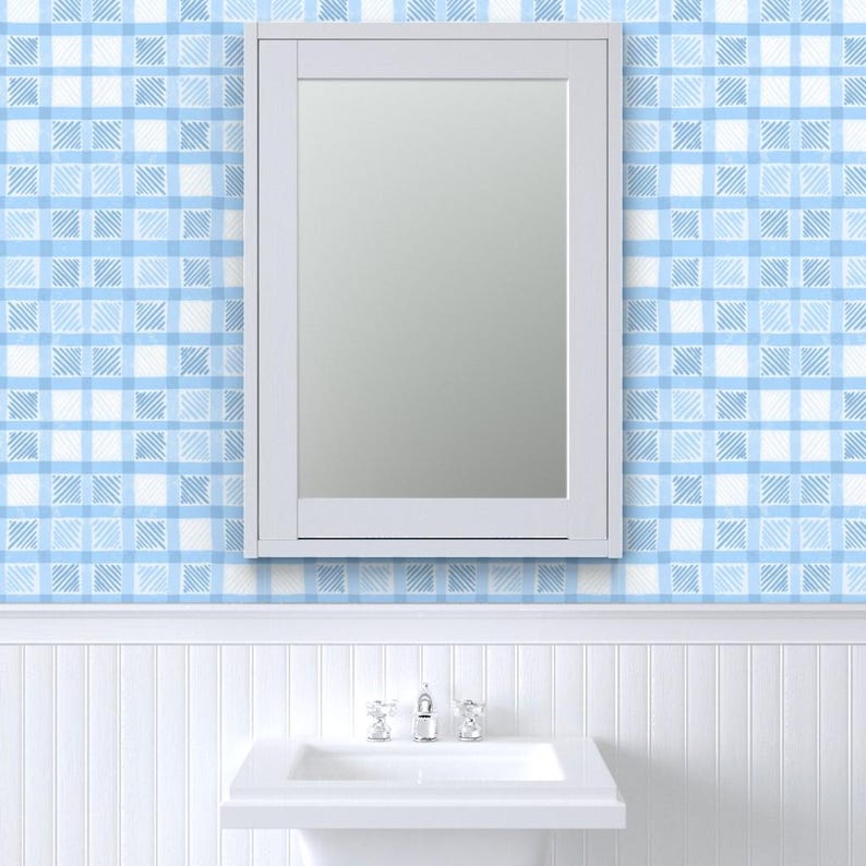 May include: A white framed mirror is mounted on a wall with blue and white plaid wallpaper. Below the mirror is a white sink with a chrome faucet. The lower wall has white vertical paneling.