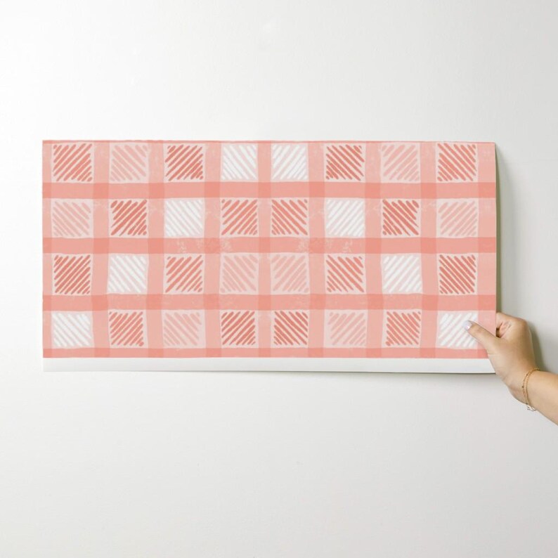 Pu&ograve; includere: Un pezzo di tessuto rettangolare con un motivo a quadri corallo e bianco. Il motivo a quadri presenta quadrati alternati di corallo e bianco, con linee diagonali all'interno di alcuni quadrati. Il tessuto &egrave; tenuto da una mano.