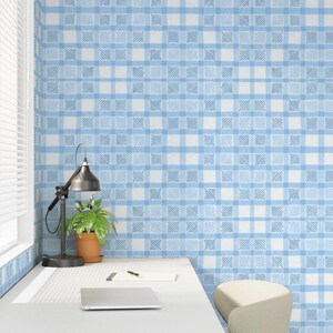 May include: A light blue and white checkered wallpaper pattern covers the wall. A desk with a laptop, pen, and notepad sits in front of the wall. A black desk lamp and a potted plant are on the desk.