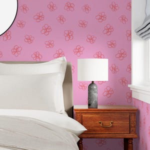 May include: A bedroom scene featuring a bed with white bedding, a wooden nightstand, and a lamp with a white shade. The lamp has a gray marble base. The wall is painted pink with a repeating floral pattern in a darker shade of pink.