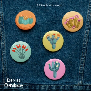 May include: Five 2.25 inch round pins featuring different cactus designs. The pins are on a blue denim background. The pins are in various colors, including orange, yellow, pink, and green.