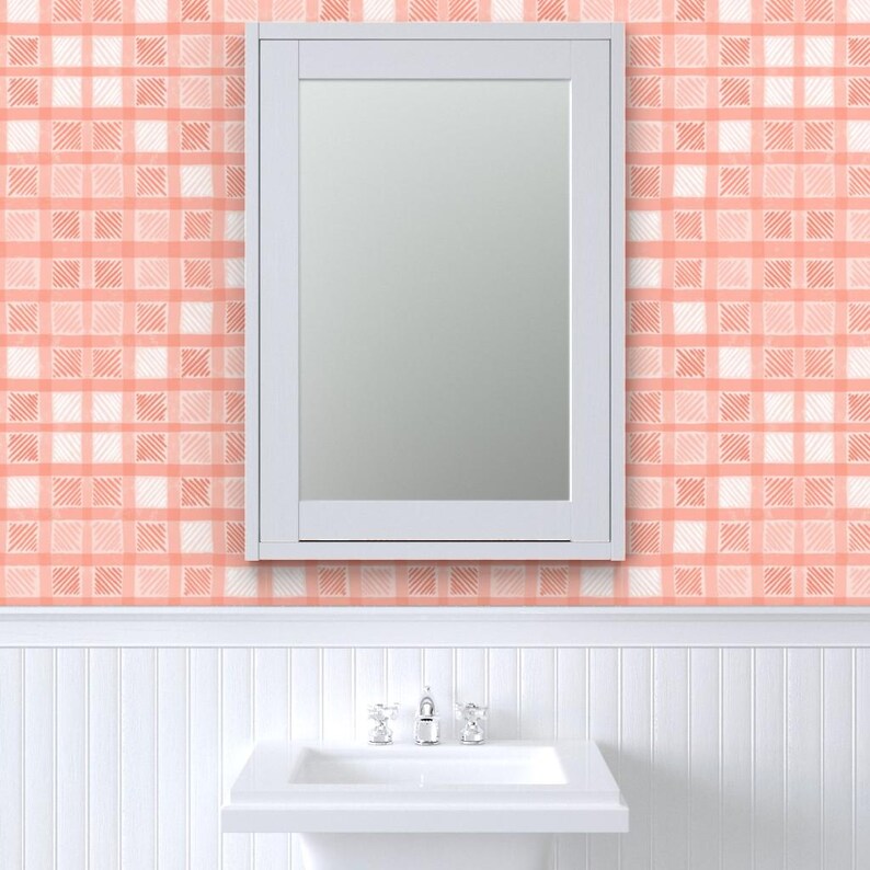 Pu&ograve; includere: Uno specchio con cornice bianca &egrave; montato su una parete con un motivo a quadri pesca e bianco. Sotto lo specchio c'&egrave; un lavandino bianco con un rubinetto cromato. Il muro ha un design a boiserie.