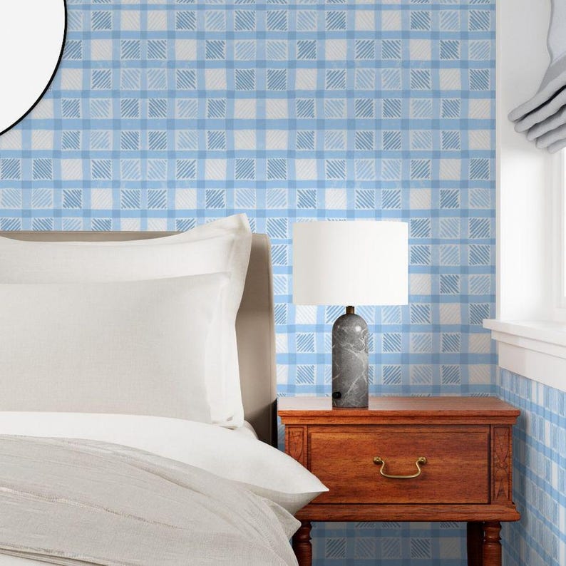 May include: A bedroom scene featuring a bed with white bedding, a wooden nightstand, and a lamp. The wall is covered in a blue and white plaid wallpaper. The lamp has a marble base and a white lampshade. The nightstand has a drawer with a brass handle.