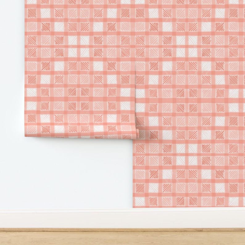 Pu&ograve; includere: Rotolo di carta da parati con motivo a quadri corallo e bianco. Il design ha un'estetica disegnata a mano, con ogni quadrato riempito di linee tratteggiate. La carta da parati &egrave; parzialmente srotolata, rivelando il motivo su una parete bianca e un pavimento in legno.