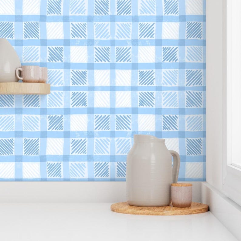 May include: A light blue and white gingham pattern wallpaper. A wooden shelf holds two small pink mugs. A gray pitcher and a small pink cup sit on a wooden tray. The scene is set against a white countertop.