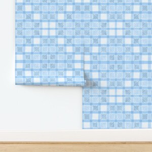 May include: A roll of blue and white checkered wallpaper. The pattern features a grid of light blue and white squares, with each square containing a textured, cross-hatched design. The wallpaper is partially unrolled, revealing the pattern against a white wall.