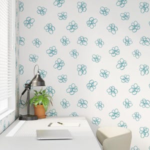 May include: A white wall adorned with a repeating pattern of teal floral designs. The room features a desk with a lamp, a potted plant, and a laptop. The wall pattern adds a decorative touch to the interior space.