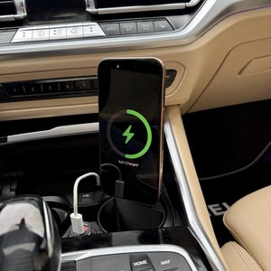 May include: A smartphone charging in a car, displaying a green charging symbol and the text "51% Charged." The phone is mounted on a black stand, connected to a white USB cable plugged into a car charger.